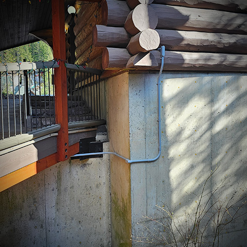 Concrete foundation wall with blue electrical conduit running up and along a wood log cabin wall with railing above.