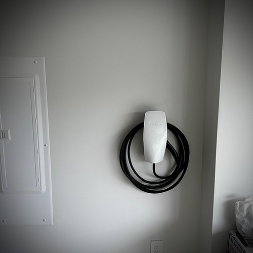 Tesla wall-mounted electric vehicle charger with coiled black cable on a plain white wall.