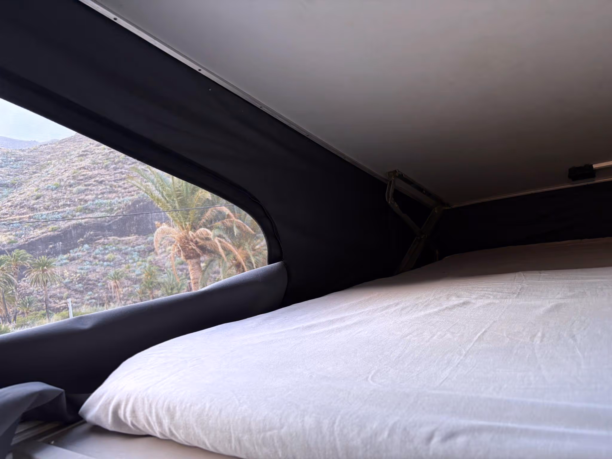 Cama montada en la camper La Negra, con vista al paisaje desde la ventana.