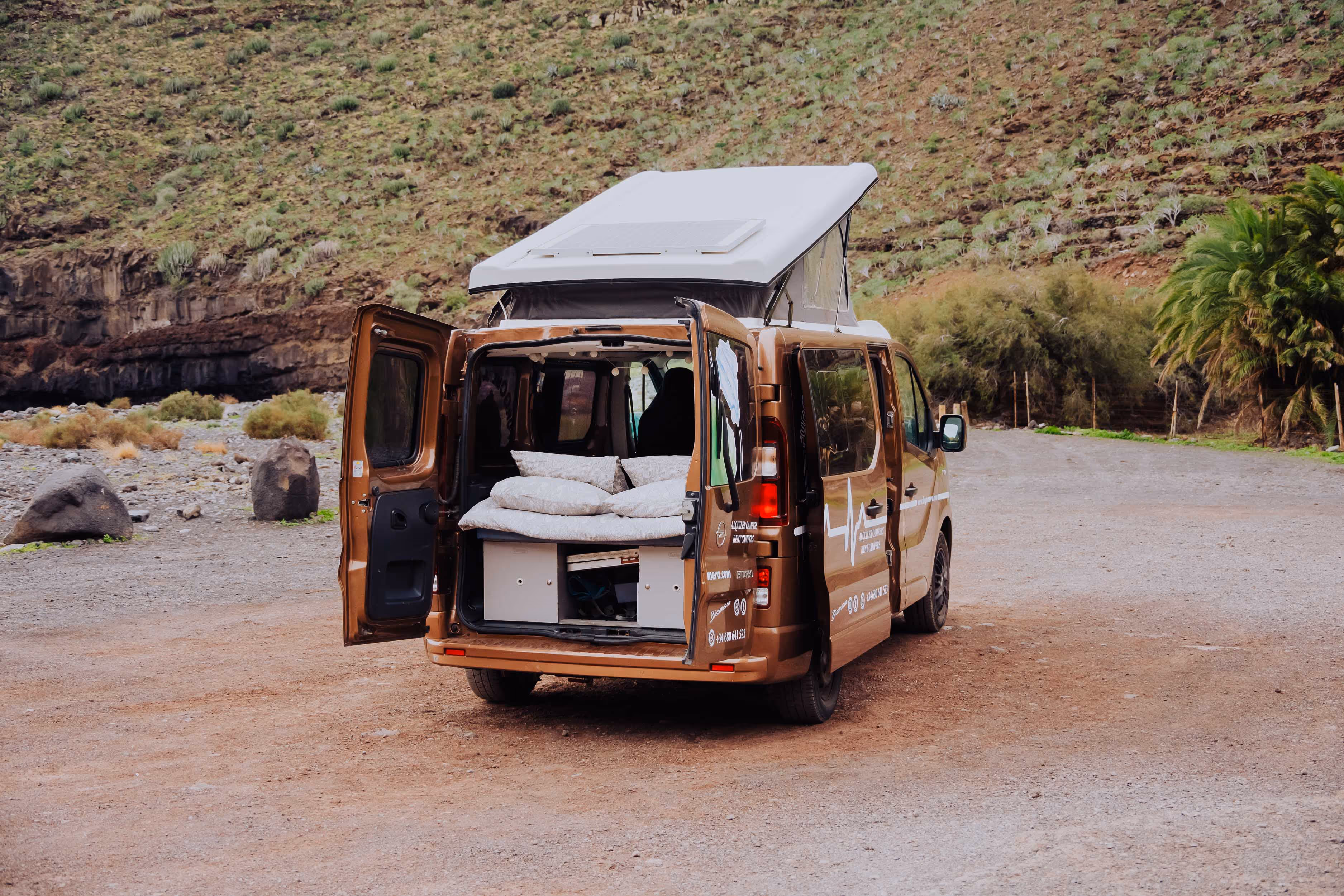 Camper Arguamul con cama y puertas abiertas en un entorno natural