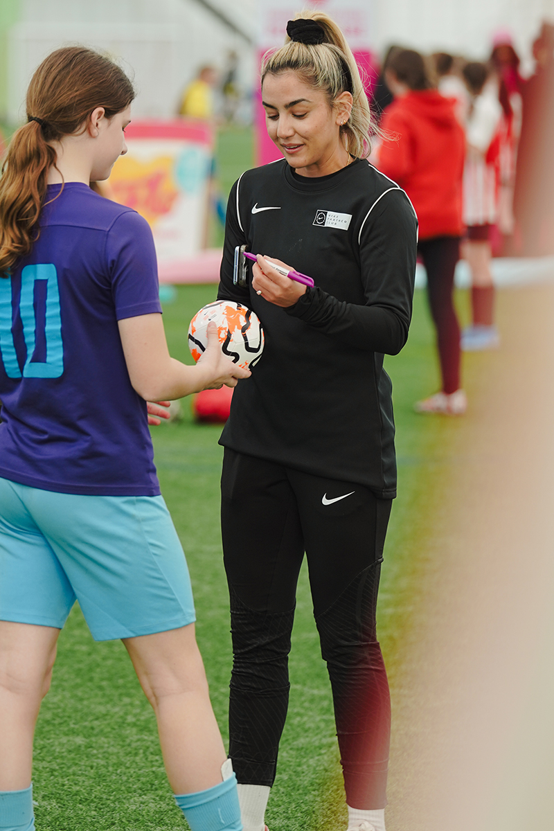 Two girls in football uniform are talking on a football field