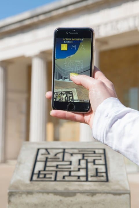 A hand holds a phone running the Actual Reality app outside the neoclassical Serpentine gallery, the screen showing a data visualisation rising from a maze plaque.
