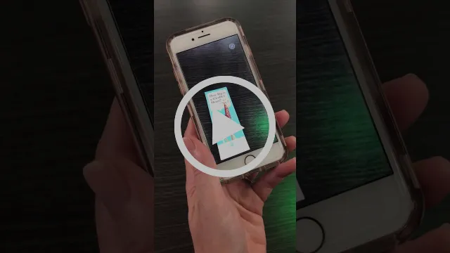 Play button over a video of a hand holding an iPhone running the Living Desert Zoo app's AR feature aimed at a printed trigger image.