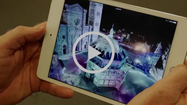 Hands holding an iPad that displays a 3D model of the Baptistery of San Giovanni and the surrounding Florence piazza, with a play button overlay.