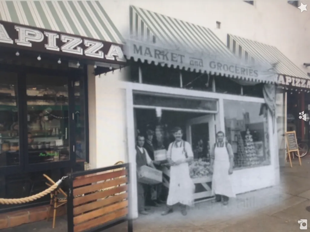 Augmented reality view blending a black and white photo of aproned grocers outside Tait's Market onto today's Little Italy pizzeria storefront.
