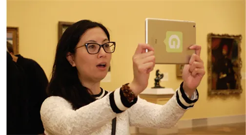 A gallery visitor gasps as she holds up a Guru-stickered tablet in front of framed paintings, the delighted reaction the post describes.