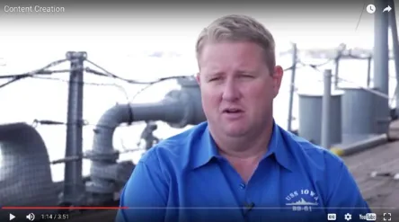 Still from the Content Creation video: a staff member in a USS IOWA BB-61 polo shirt speaking on the ship's deck about working with Guru.