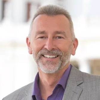 Headshot of Nik Honeysett, smiling in a grey blazer and purple shirt, opening Guru's interview series with museum digital leaders.