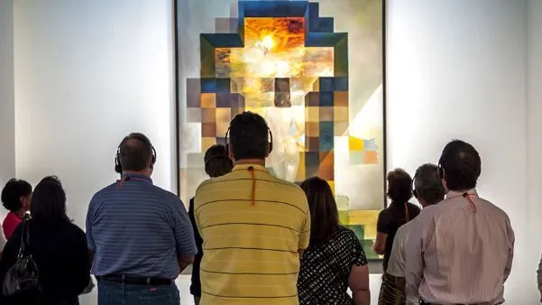 Group of visitors seen from behind, several in headphones, standing before a large mosaic-like Dali painting during a gallery audio tour.