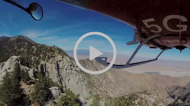 Play button over a 360 video shot from beneath a Palm Springs Aerial Tramway car, looking down at granite cliffs and the desert valley floor.