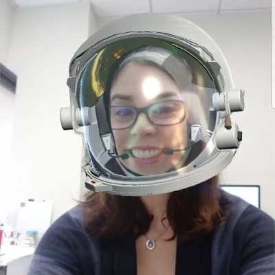 Smiling woman wearing a virtual astronaut helmet from Space Center Houston's app selfie filter, photographed at her desk.