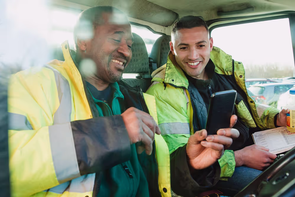 Two men in work coats sit in the cab of a truck together