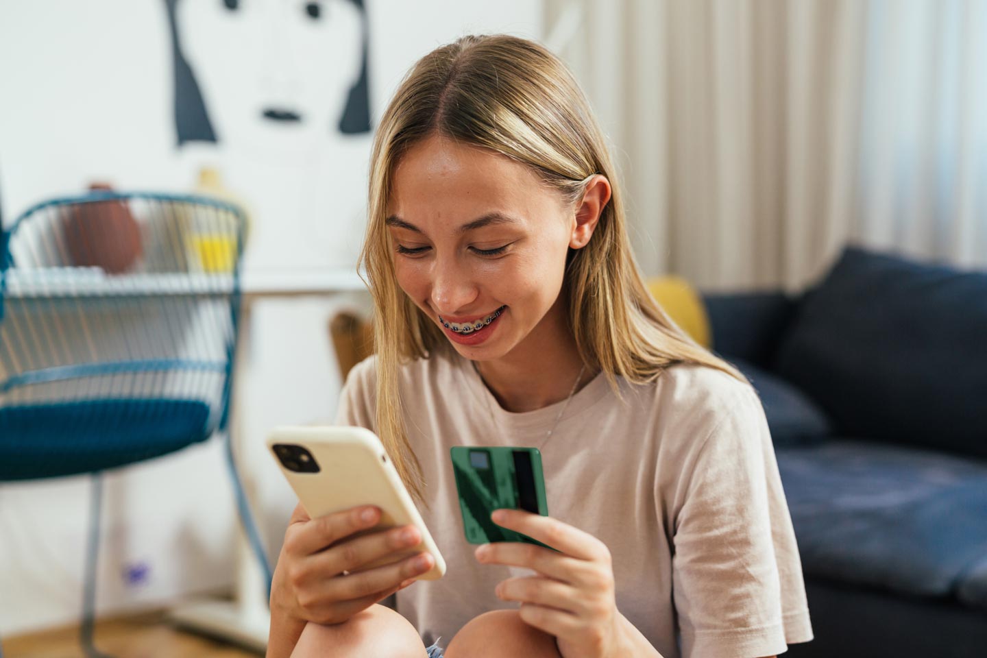 Young teen girl smiles while holding a debit card and looking at her phone.