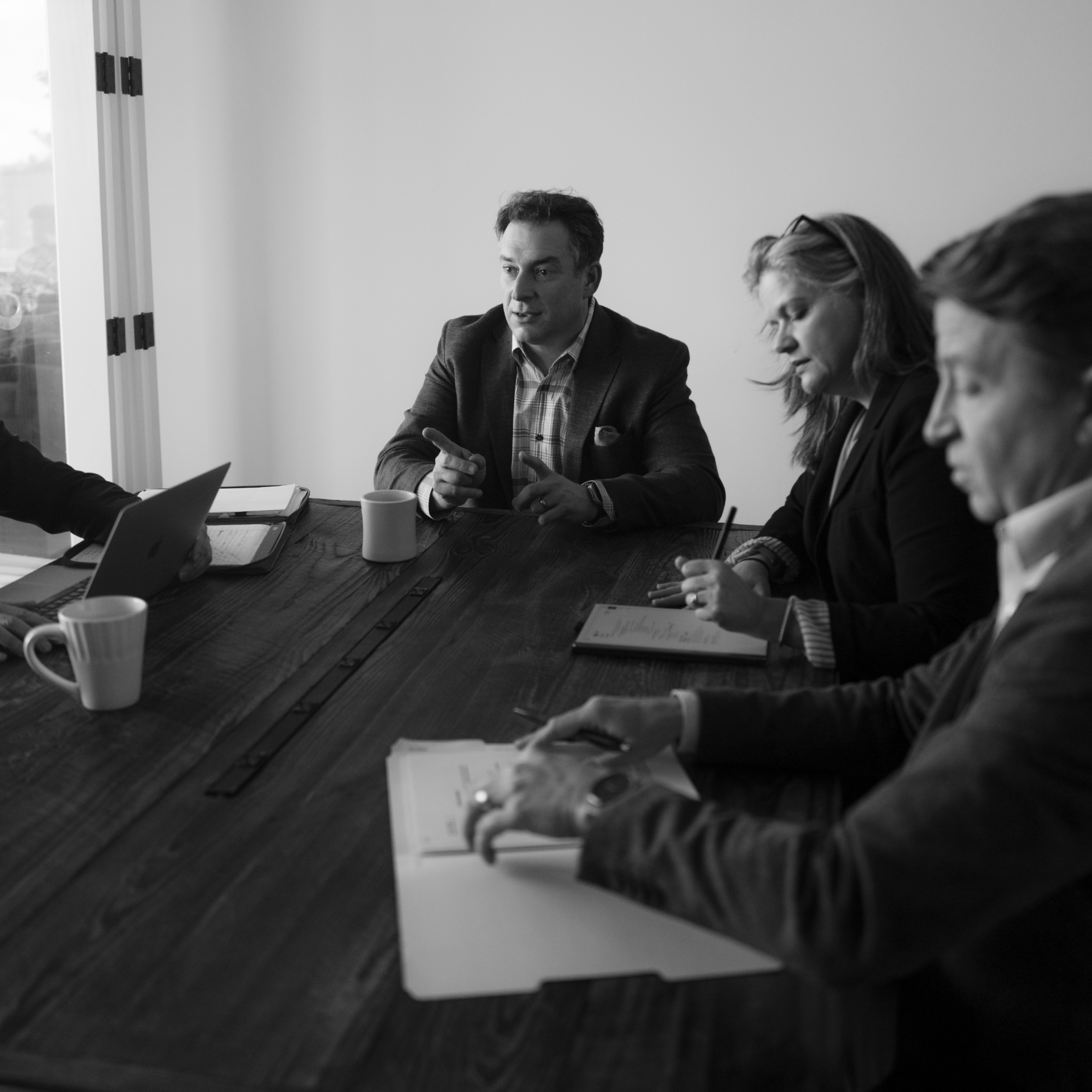 B&W image of 3 employees around a conference table with documents on the table
