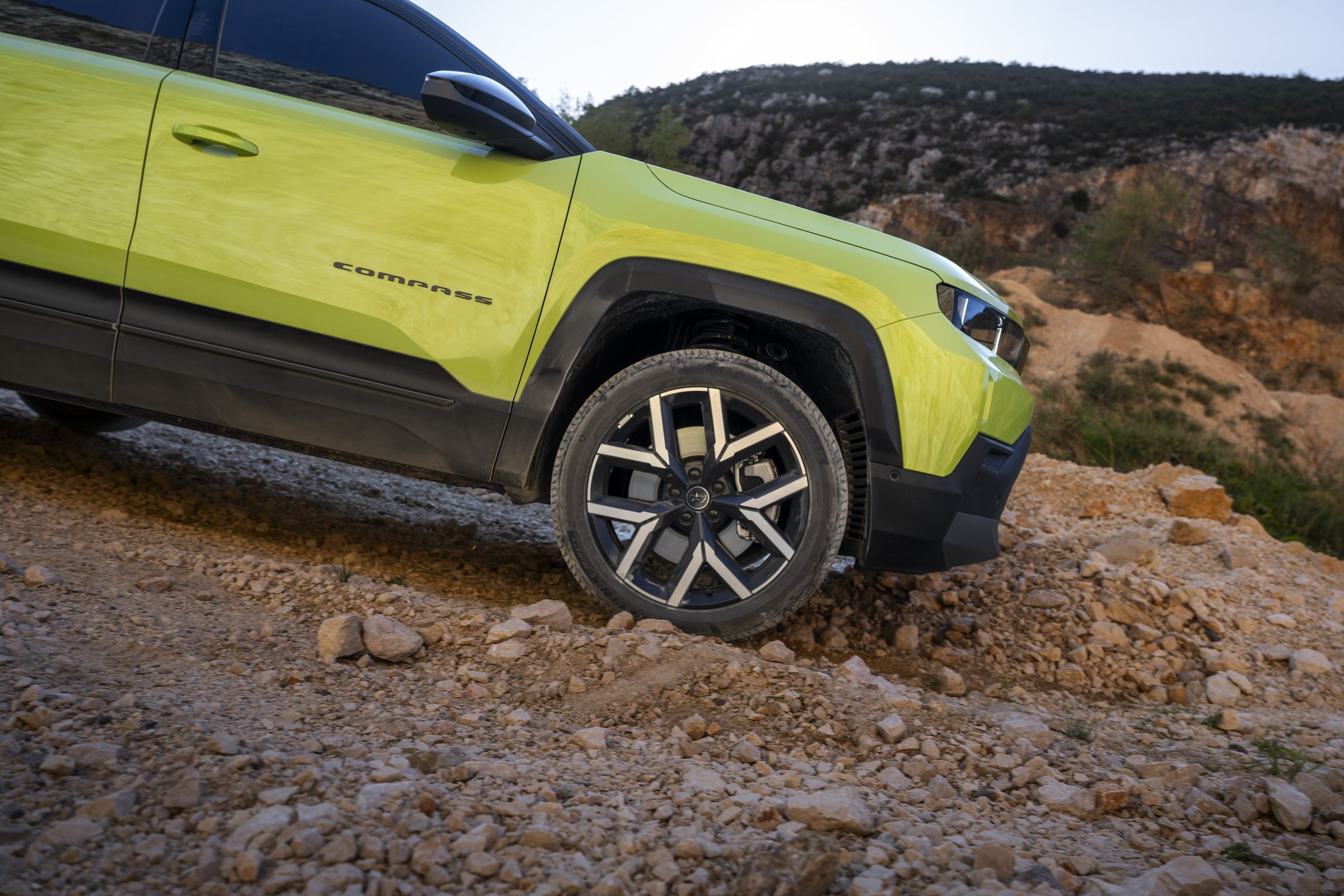 Neuer Jeep Compass e-Hybrid im Gelände auf grobem Fels, Detail Vorderrad