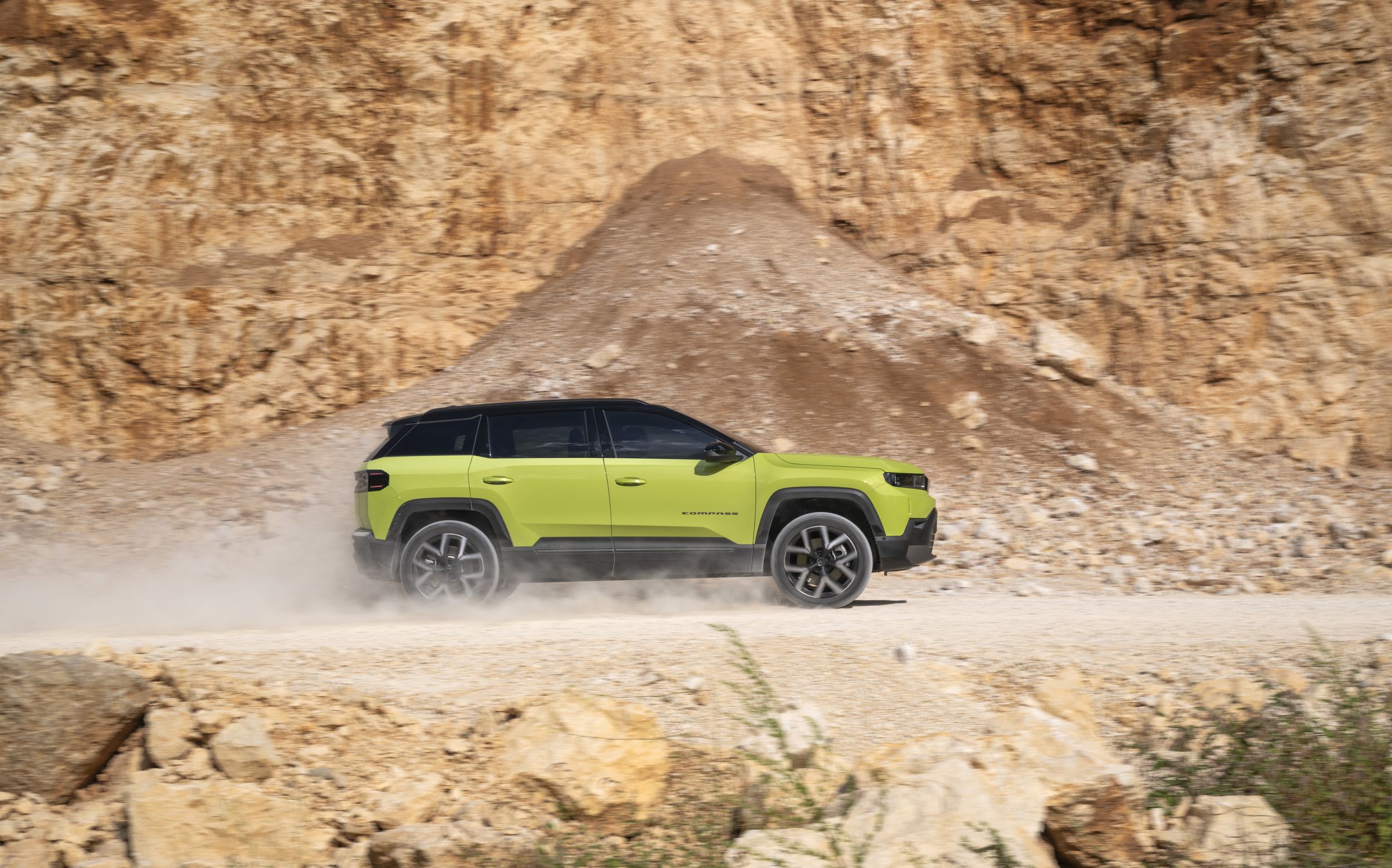 Neuer Jeep Compass e-Hybrid in Hawaii Grün fährt seitlich durch einen staubigen Steinbruch