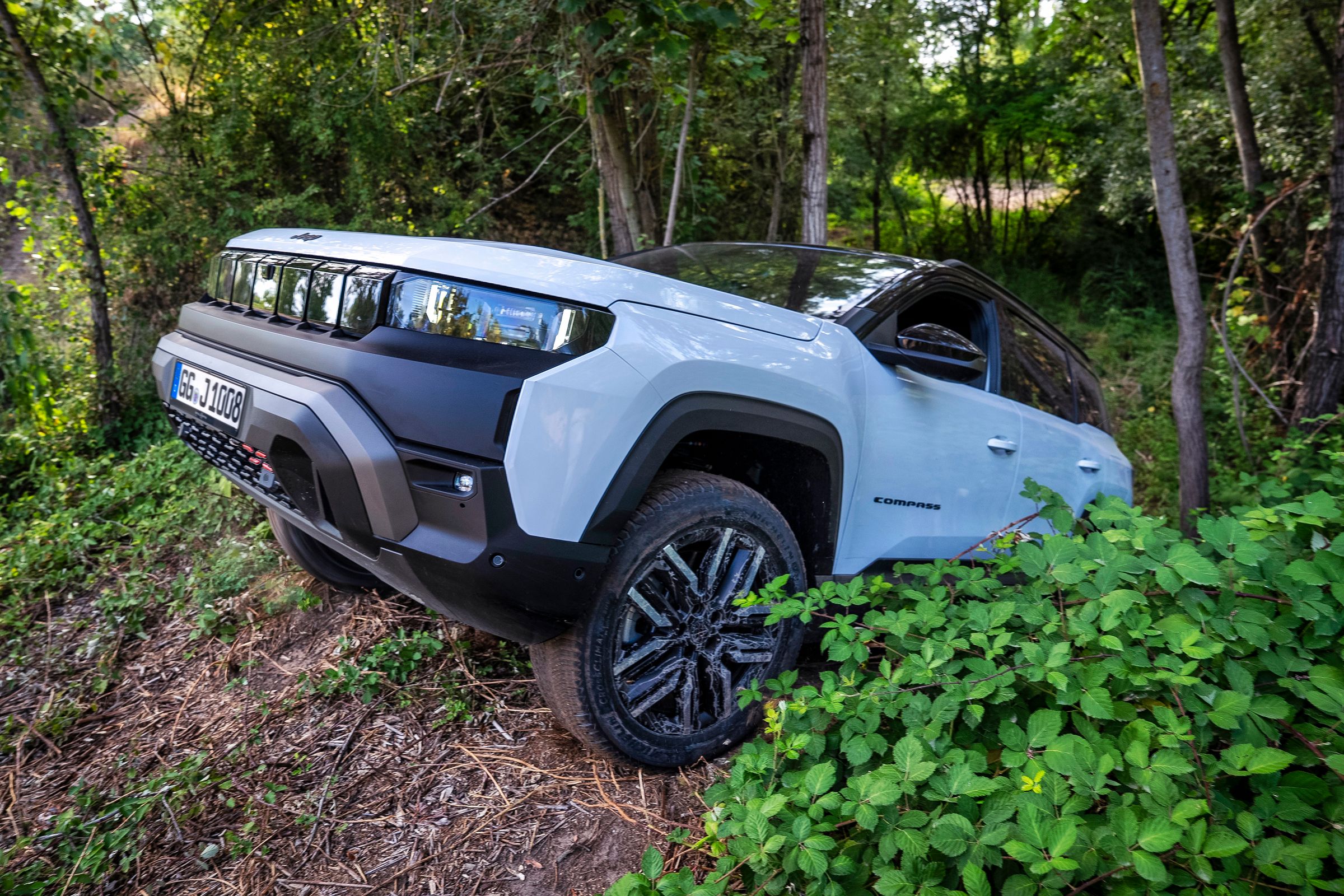 Neuer Jeep Compass 4xe Elektro fährt einen bewaldeten Offroad-Hang hinauf