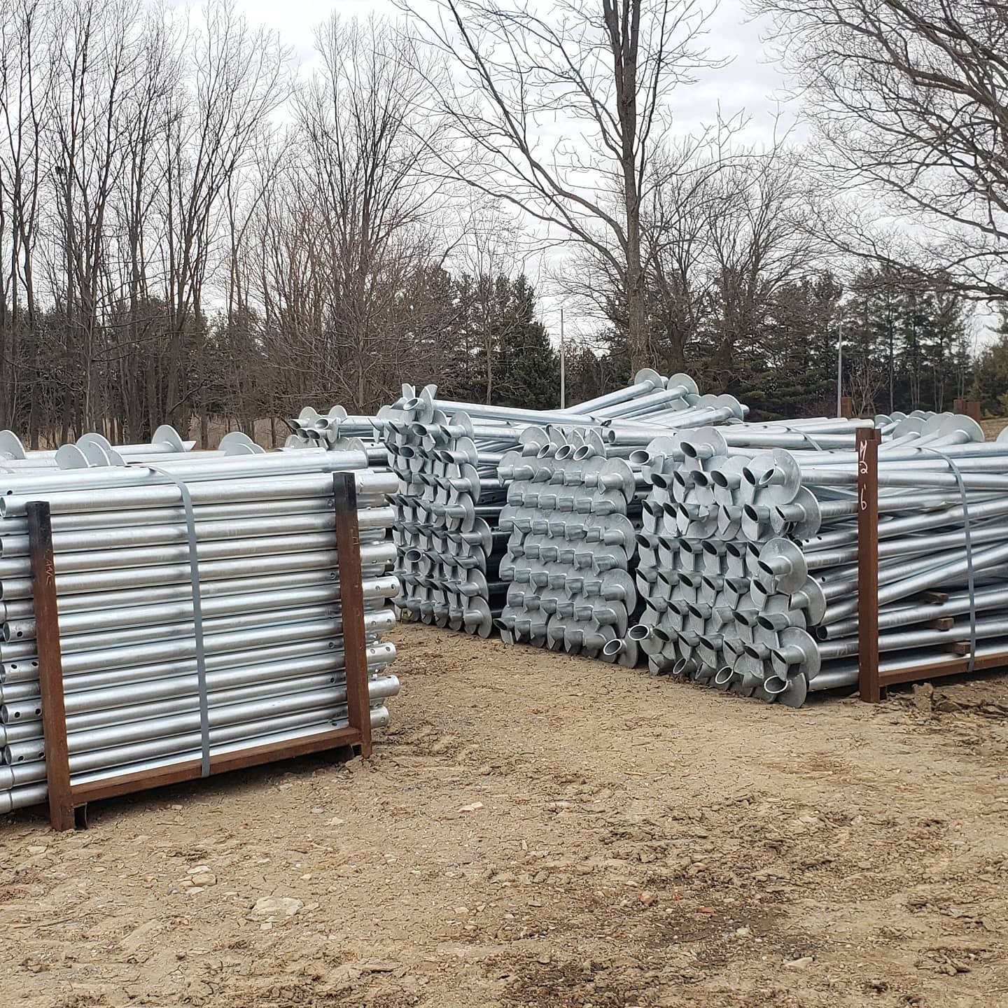 Stacks of galvanized steel helical piles with circular helix plates bundled and stored outdoors at a construction yard