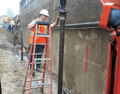 Worker using ladder for wall installation with helical pile foundations