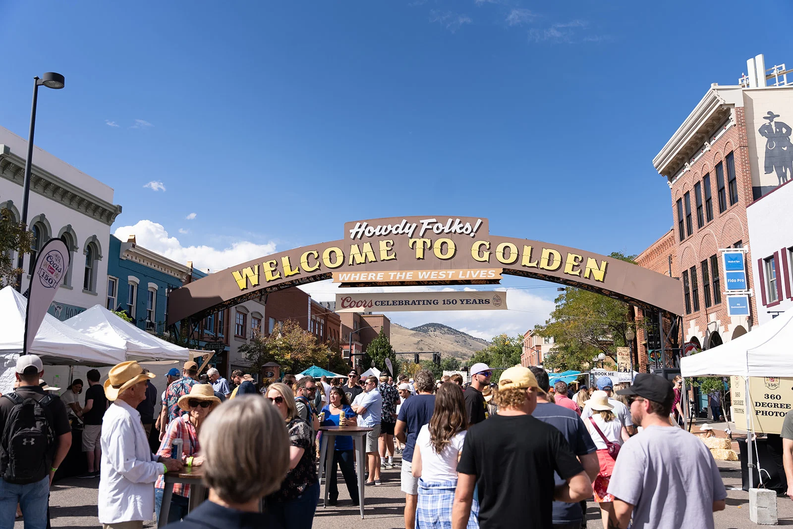Crowds pass beneath the Welcome to Golden arch at Imprint's citywide Coors Brewery 150th Celebration