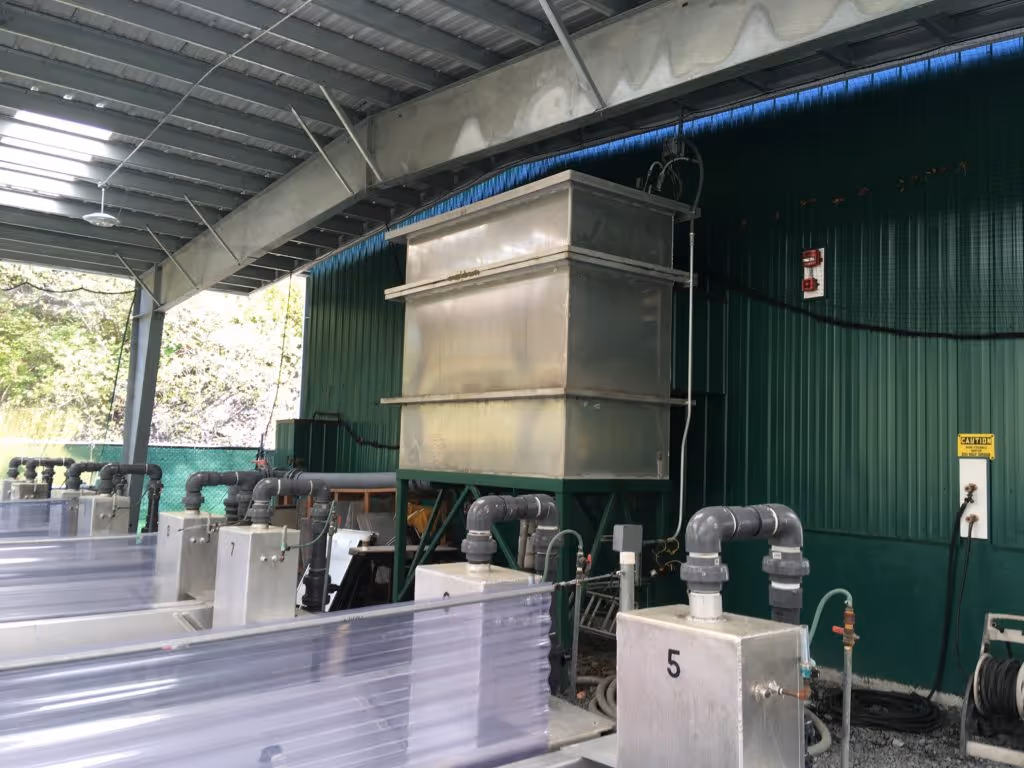 Industrial setup with numbered metallic water treatment units and large tank under a metal roof structure.