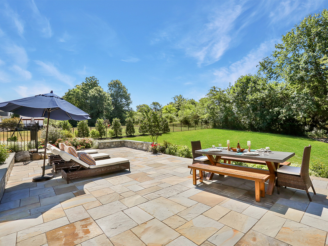 Gorgeous backyard retreat with stone patio, lounge chairs, brick wall, outdoor grill station, and luscious grass. This project was designed and built by Rossen Landscape.