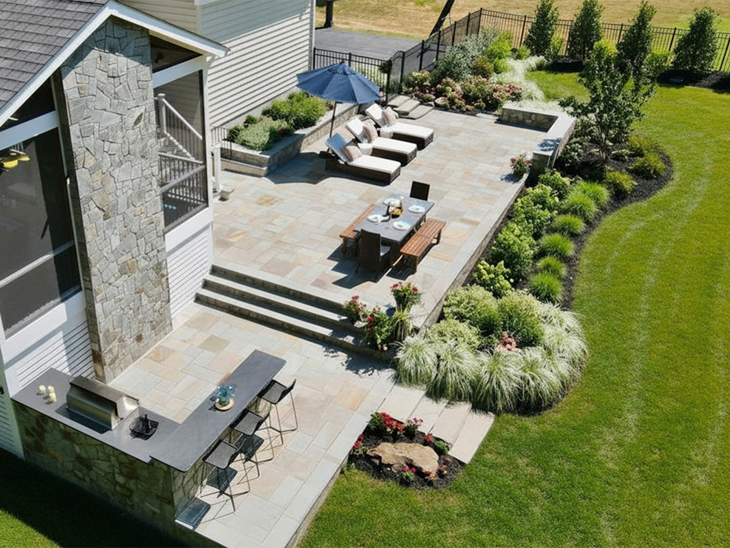 Gorgeous backyard retreat with stone patio, lounge chairs, brick wall, outdoor grill station, and luscious grass. This project was designed and built by Rossen Landscape.