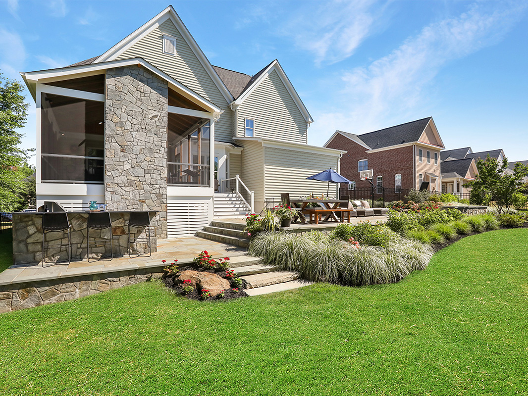 Gorgeous backyard retreat with stone patio, lounge chairs, brick wall, outdoor grill station, and luscious grass. This project was designed and built by Rossen Landscape.