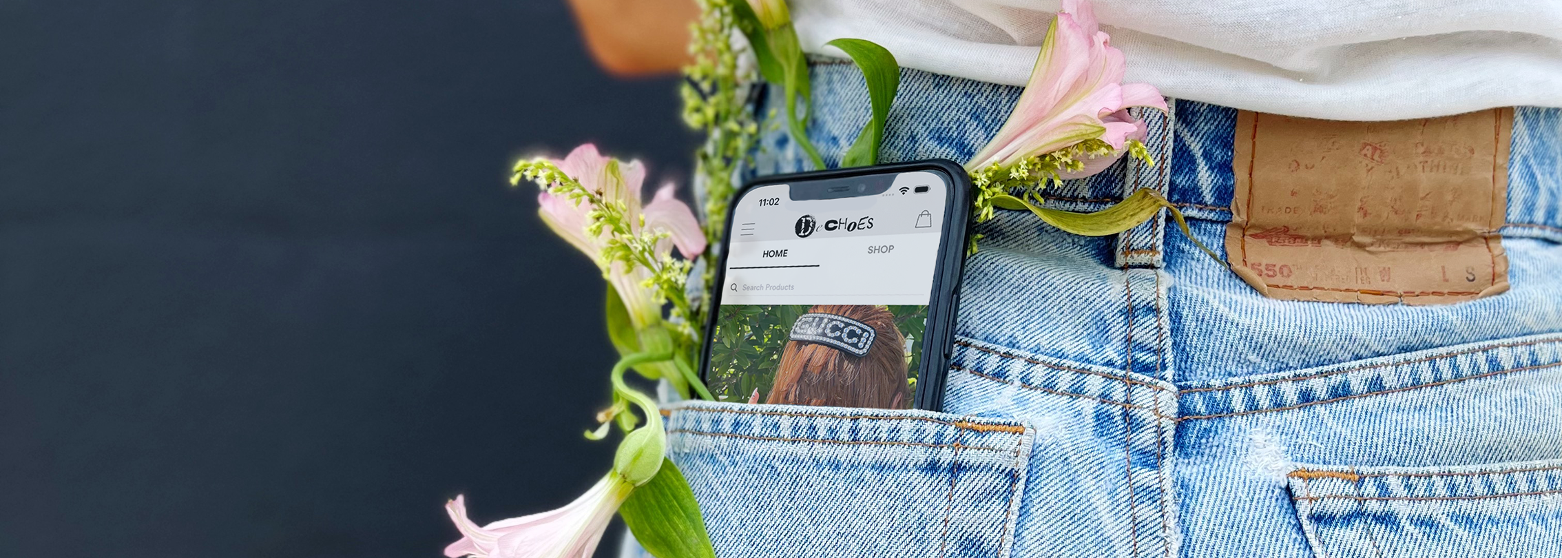 A mobile phone in the back pocket of a woman wearing jeans, with a flower in the pocket with the phone