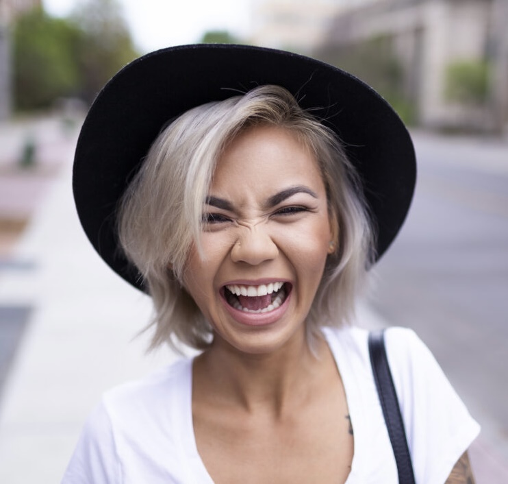 A young woman with blonde hair in a black wide brimmed hat laughing