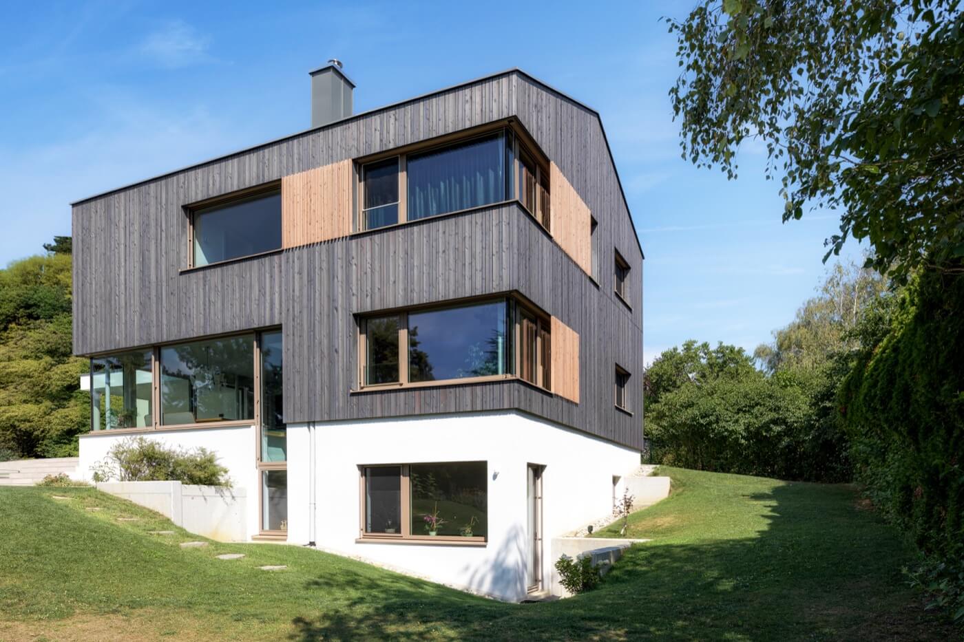 Fertigteilhaus mit einer auffälligen Kombination aus dunkler Holzfassade und weißem Putzsockel.