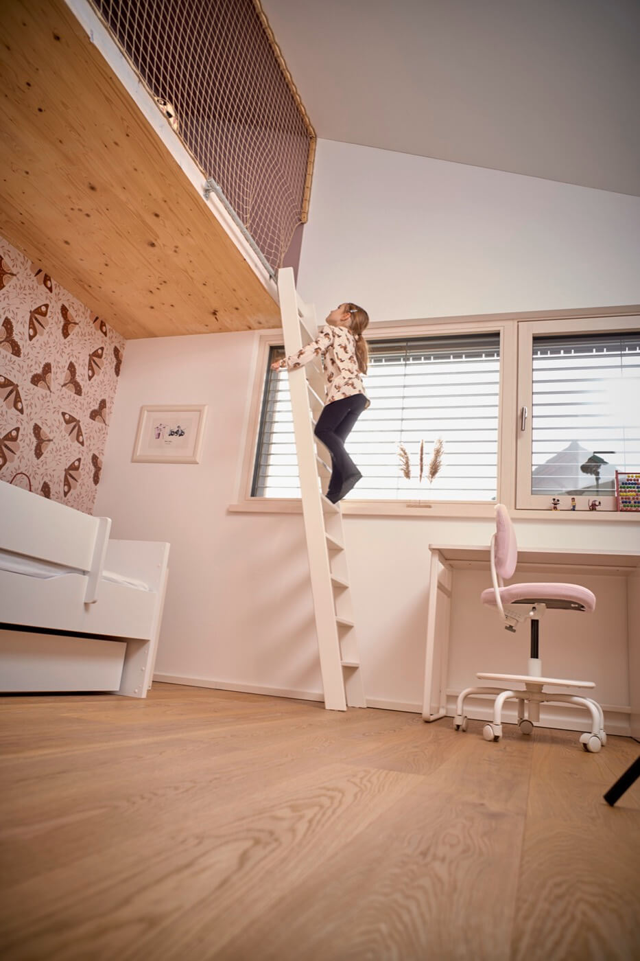 Ein Mädchen klettert in einem Kinderzimmer auf einer weißen Leiter hoch, um zu einer Hochebene zu gelangen.