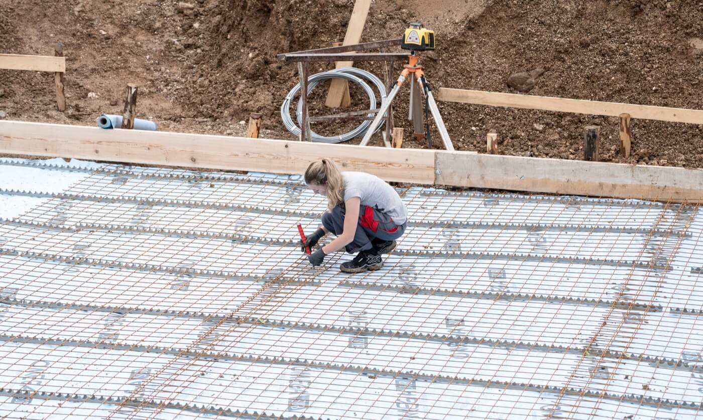Eine Frau arbeitet auf einer Baustelle an der Bewehrung für eine Bodenplatte.