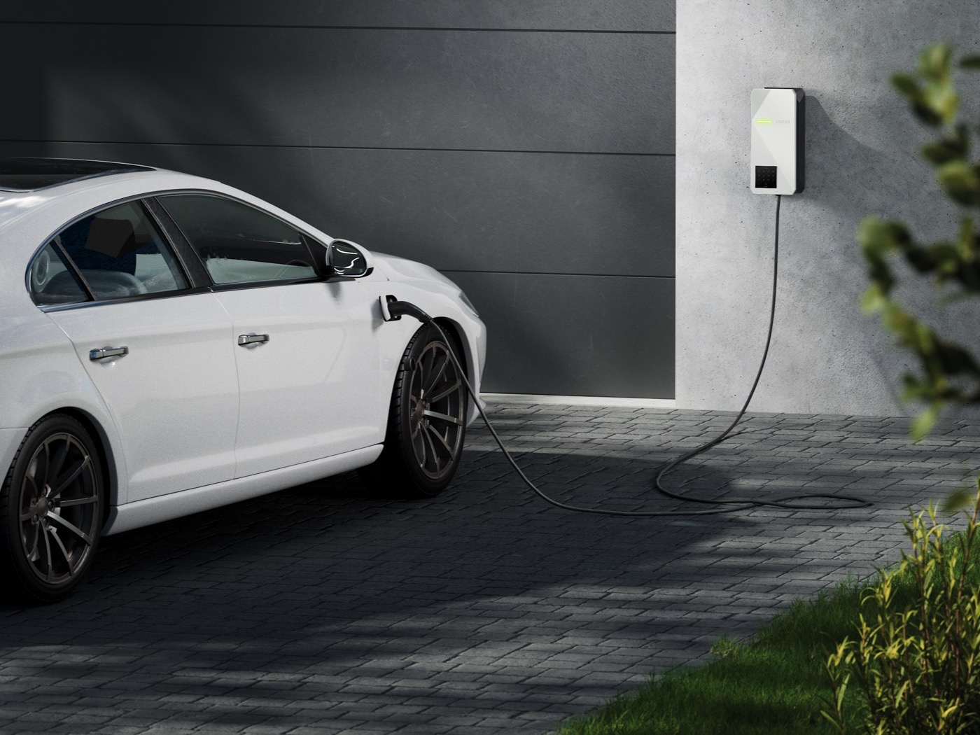 Ein weißes Elektroauto ist vor einer Garage an einer Wallbox angeschlossen und lädt Strom.
