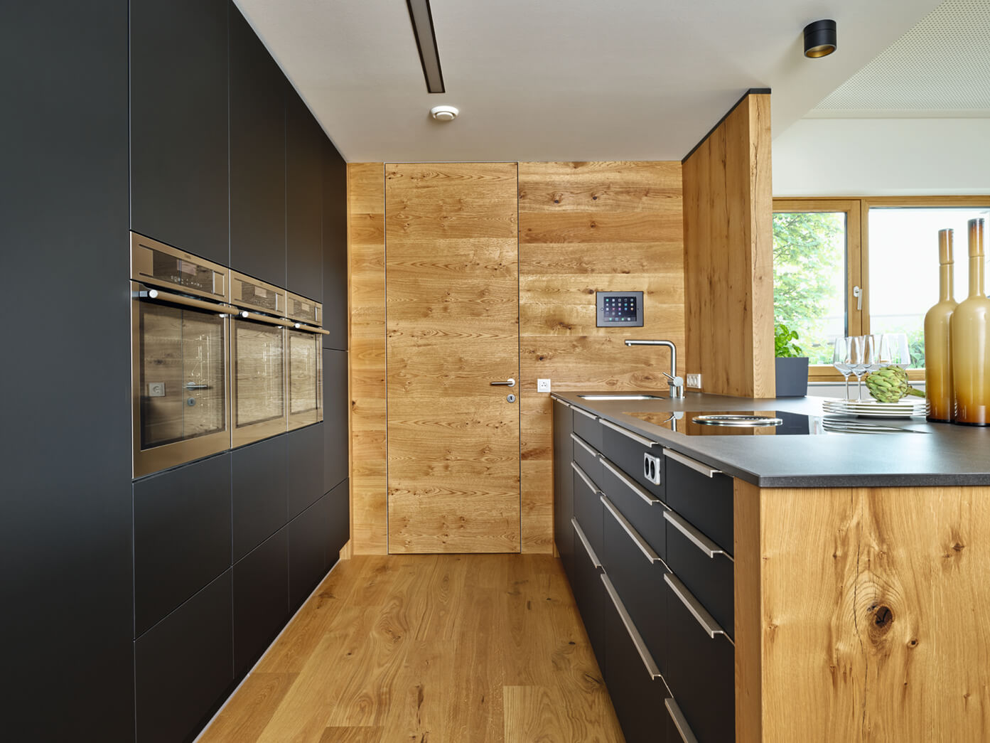 Designerküche, die durch einen starken Kontrast zwischen mattschwarzen Oberflächen und warmen, astigen Eichenholzelementen besticht.
