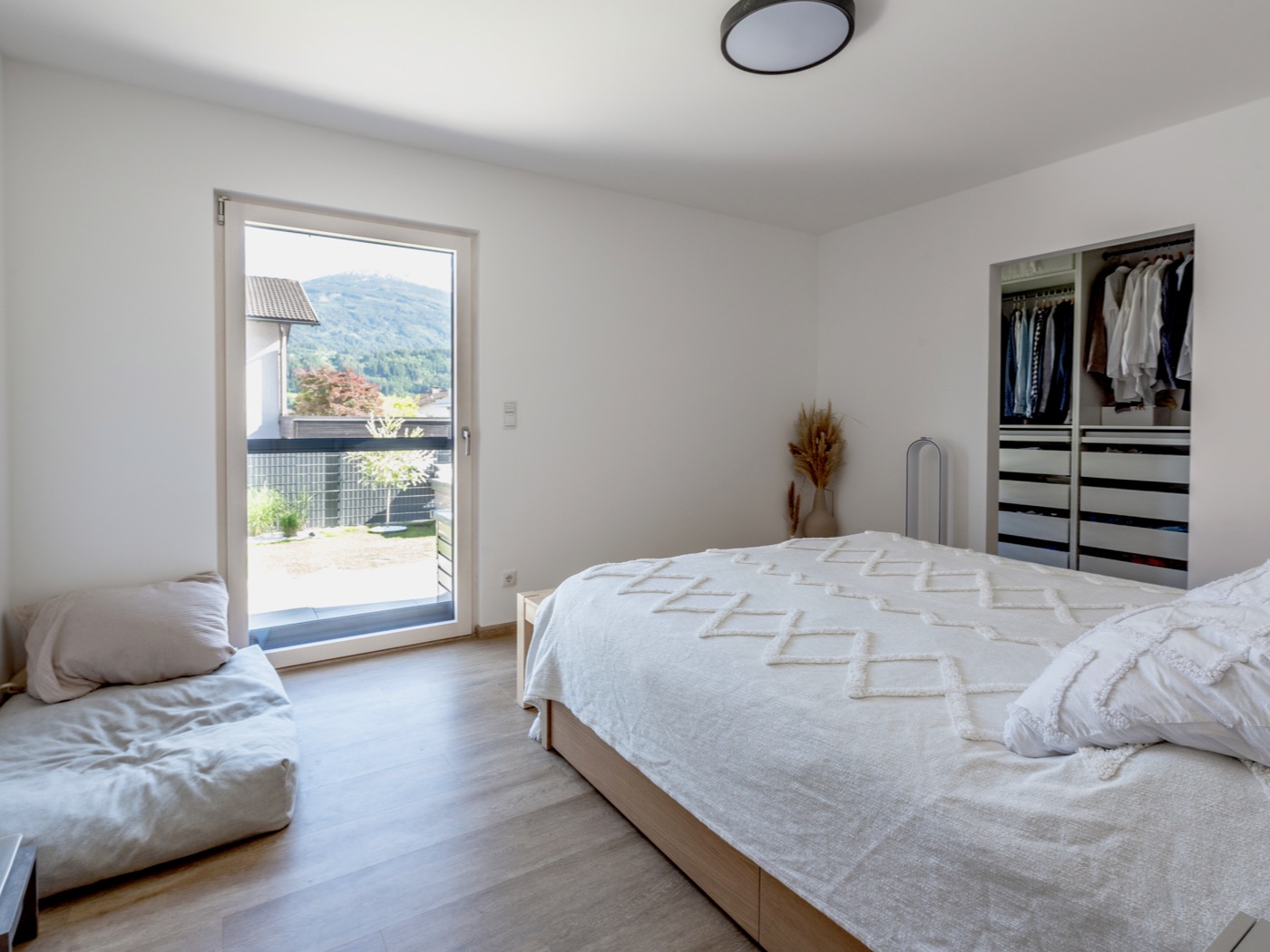 Schlafzimmer von HARTL HAUS mit hellem Holzboden, einem großen Fenster und einem offenen Ankleidebereich