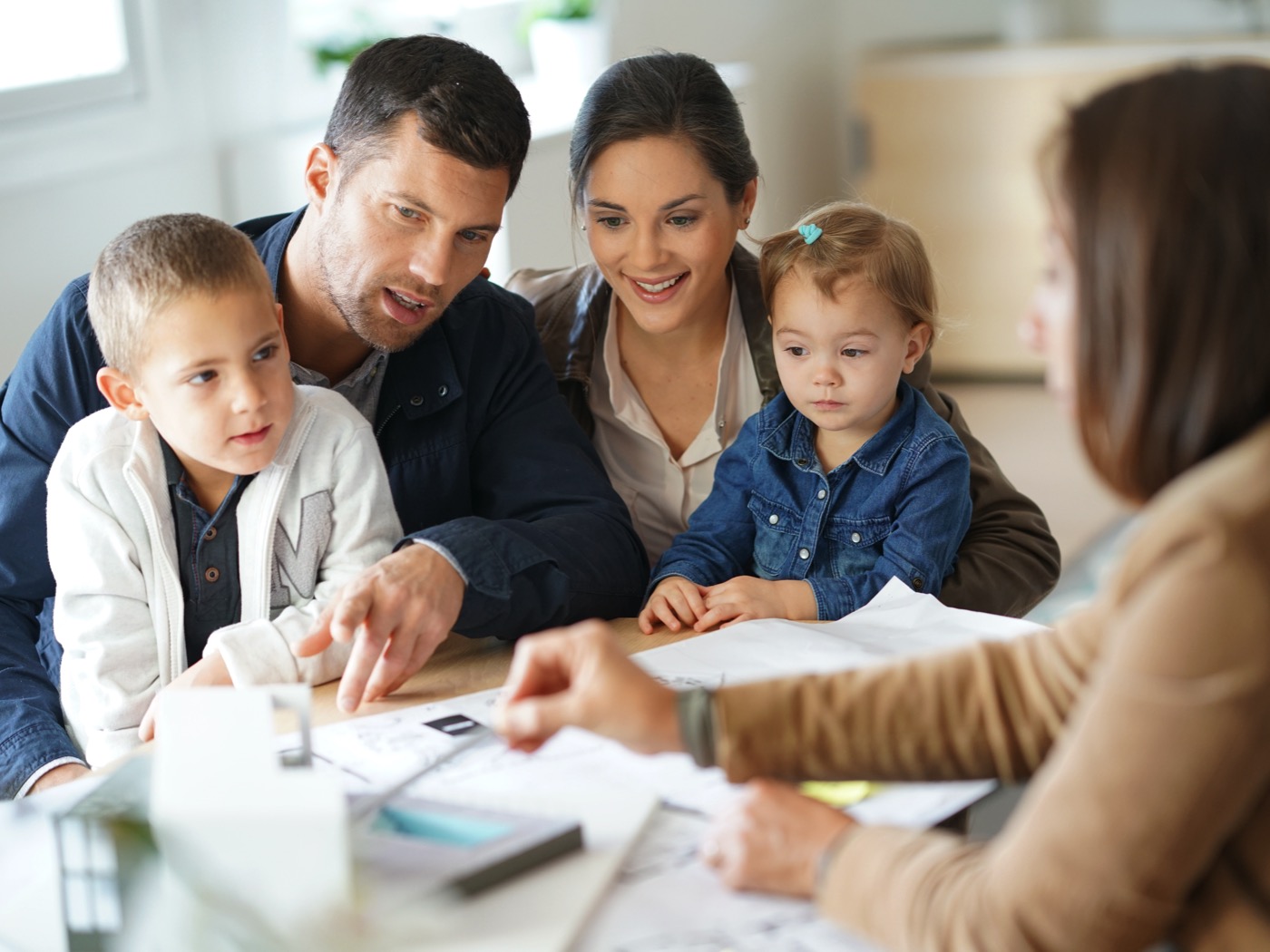 Eine Familie bespricht mit einer Beraterin Baupläne an einem Tisch.
