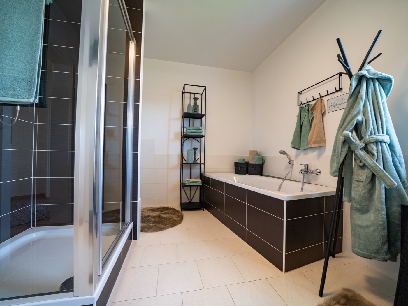 Badezimmer mit Duschkabine, Badewanne und dunklen Fliesenakzenten eines Fertigteilhauses vom Hersteller Wolf Haus.