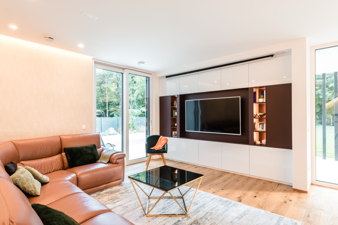 Wohnzimmer eines Hauses von Lumar Haus mit großer Leder-Eckcouch und maßgefertigter TV-Wand.