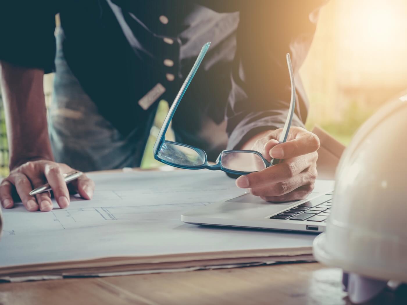 Eine Person beugt sich über einen Arbeitstisch mit Bauunterlagen.