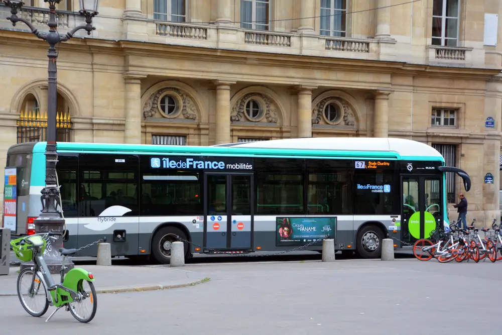 Bus hybride RATP de couleur gris et turquoise, stationné dans une rue de Paris avec des vélos en libre-service au premier plan.