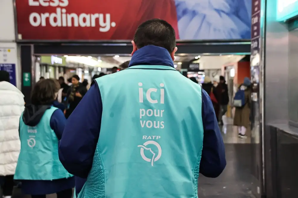 Agent de gare RATP portant un gilet avec l'inscription "ici pour vous", illustrant son rôle d'accueil et d'assistance.