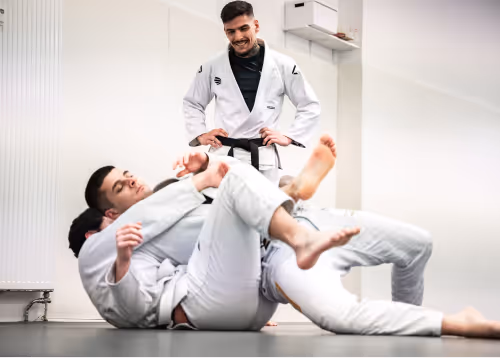 Two athletes in white gis performing grappling techniques during a Jiu-Jitsu class