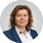 Professional headshot of a woman with curly light brown hair wearing a blue blazer and white blouse against a light background.