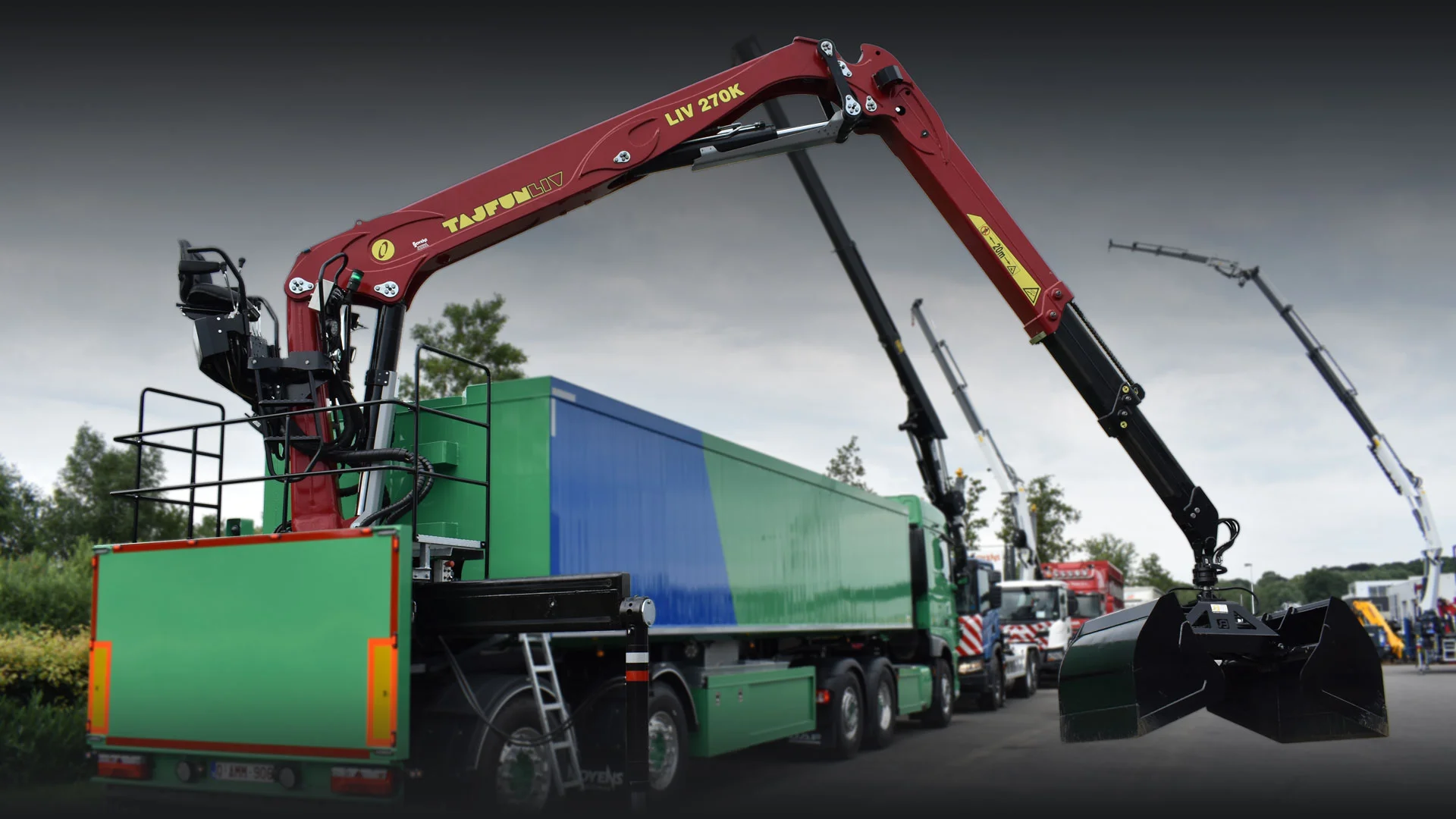 Green and blue heavy-duty truck equipped with a red Tajfun LIV 270K crane with claw attachment.