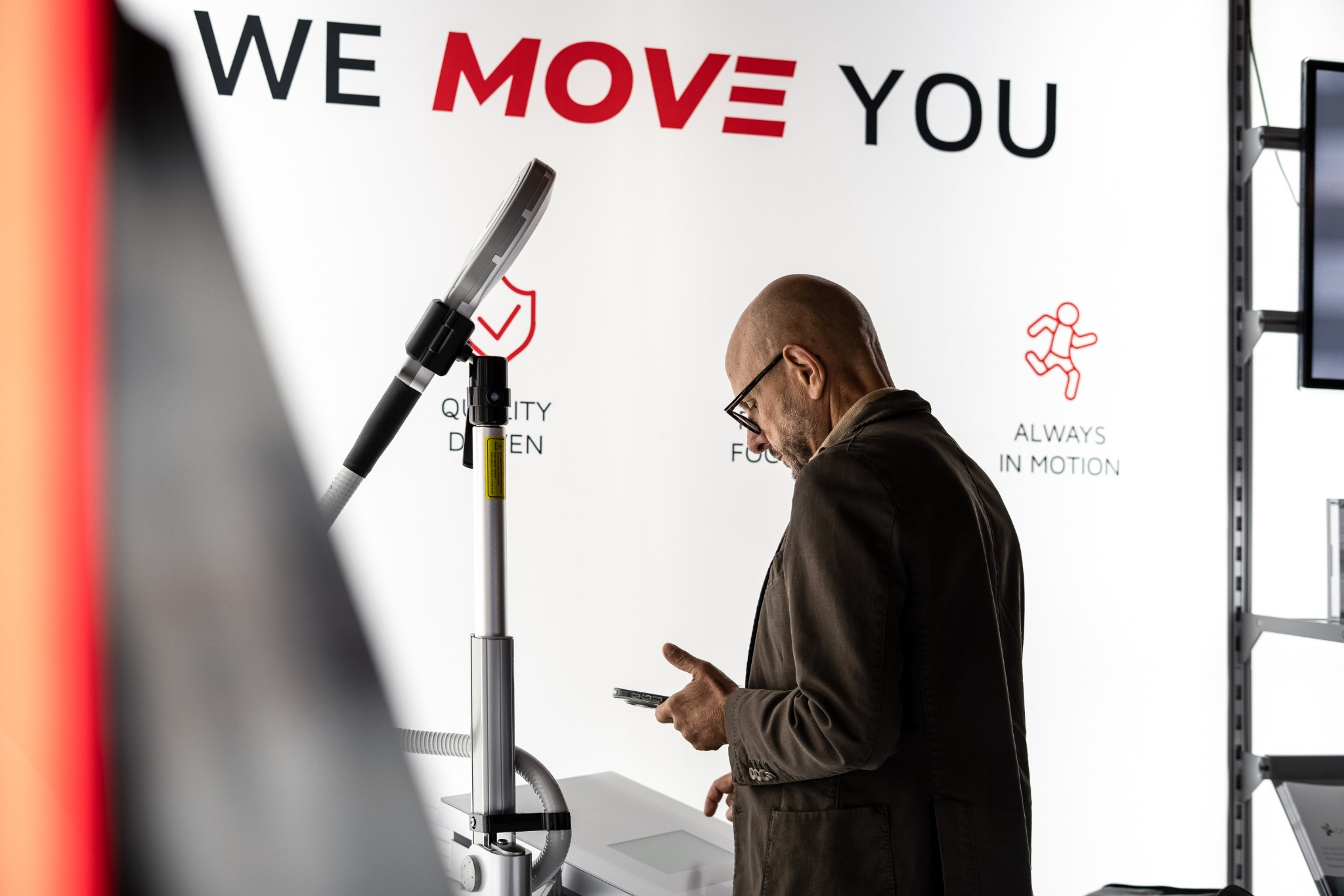 Besucher betrachtet sein Smartphone neben einem medizinischen Gerät am Haemo-Pharma-Messestand.