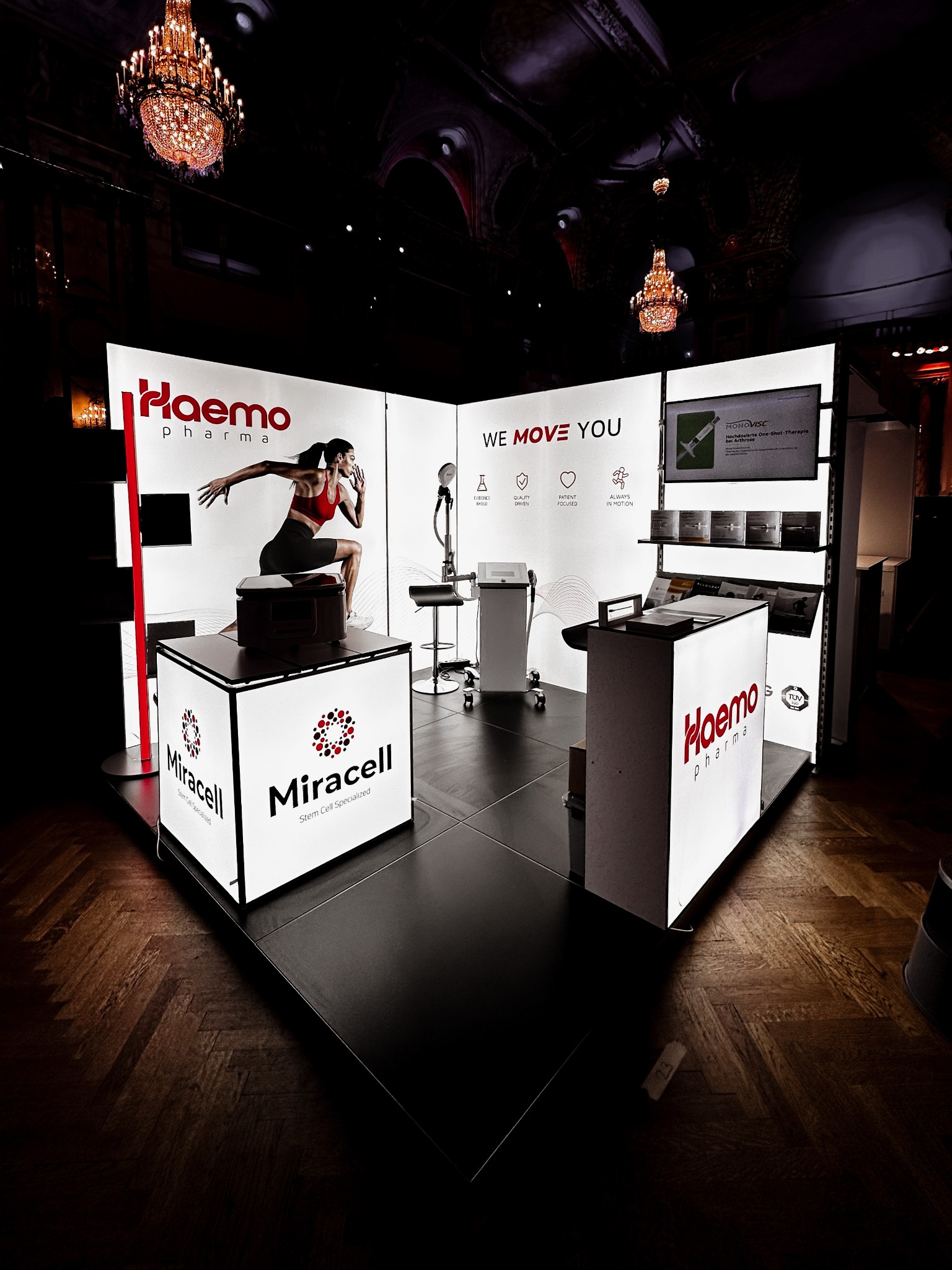 Beleuchteter Messestand von Haemo Pharma und Miracell in einem eleganten Veranstaltungssaal mit Kronleuchtern.