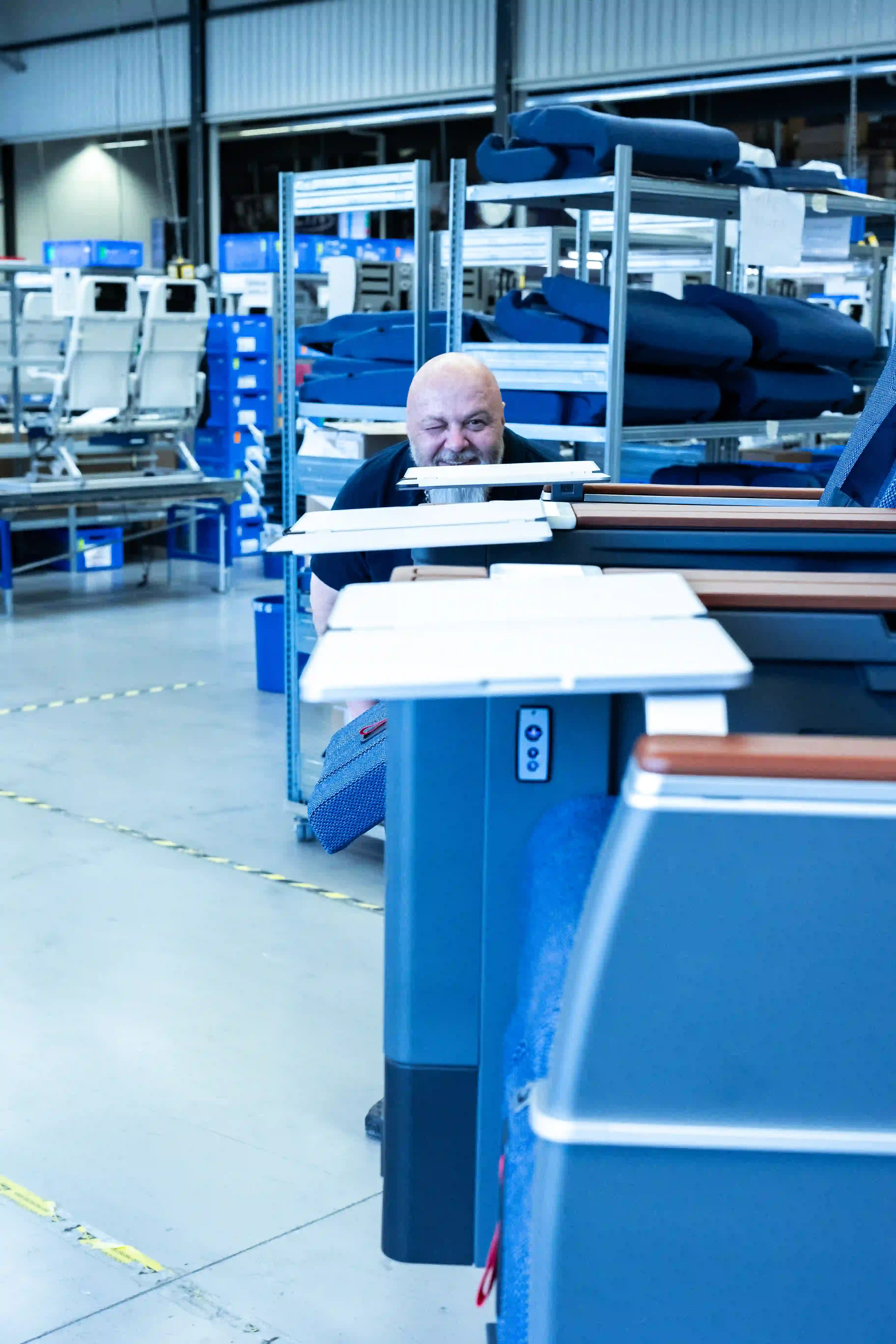 Mann schaut zwischen Reihen von blauen Flugzeugsitzen in einer Fabrikhalle.