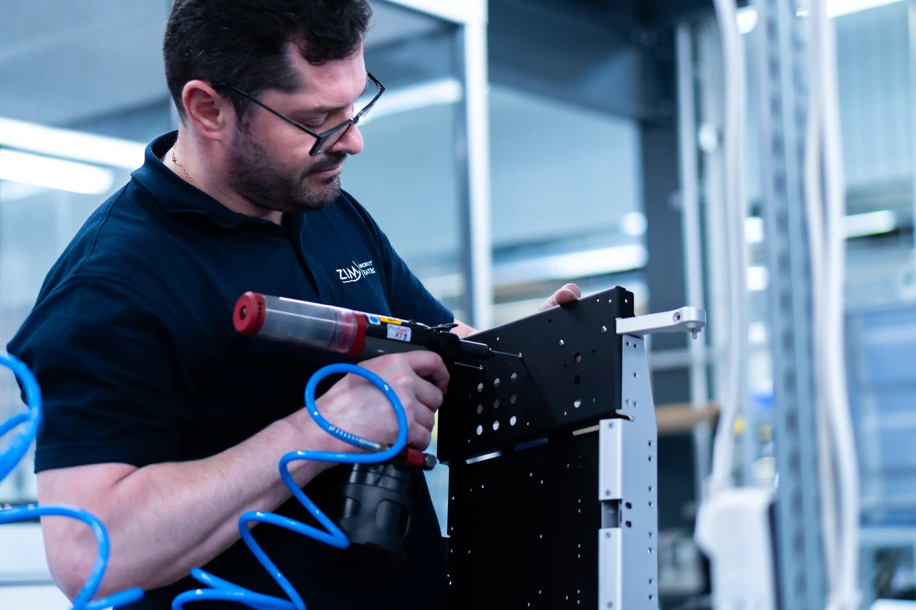 Mann mit Brille montiert schwarzen Metallrahmen mit Druckluftwerkzeug in Werkstatt.
