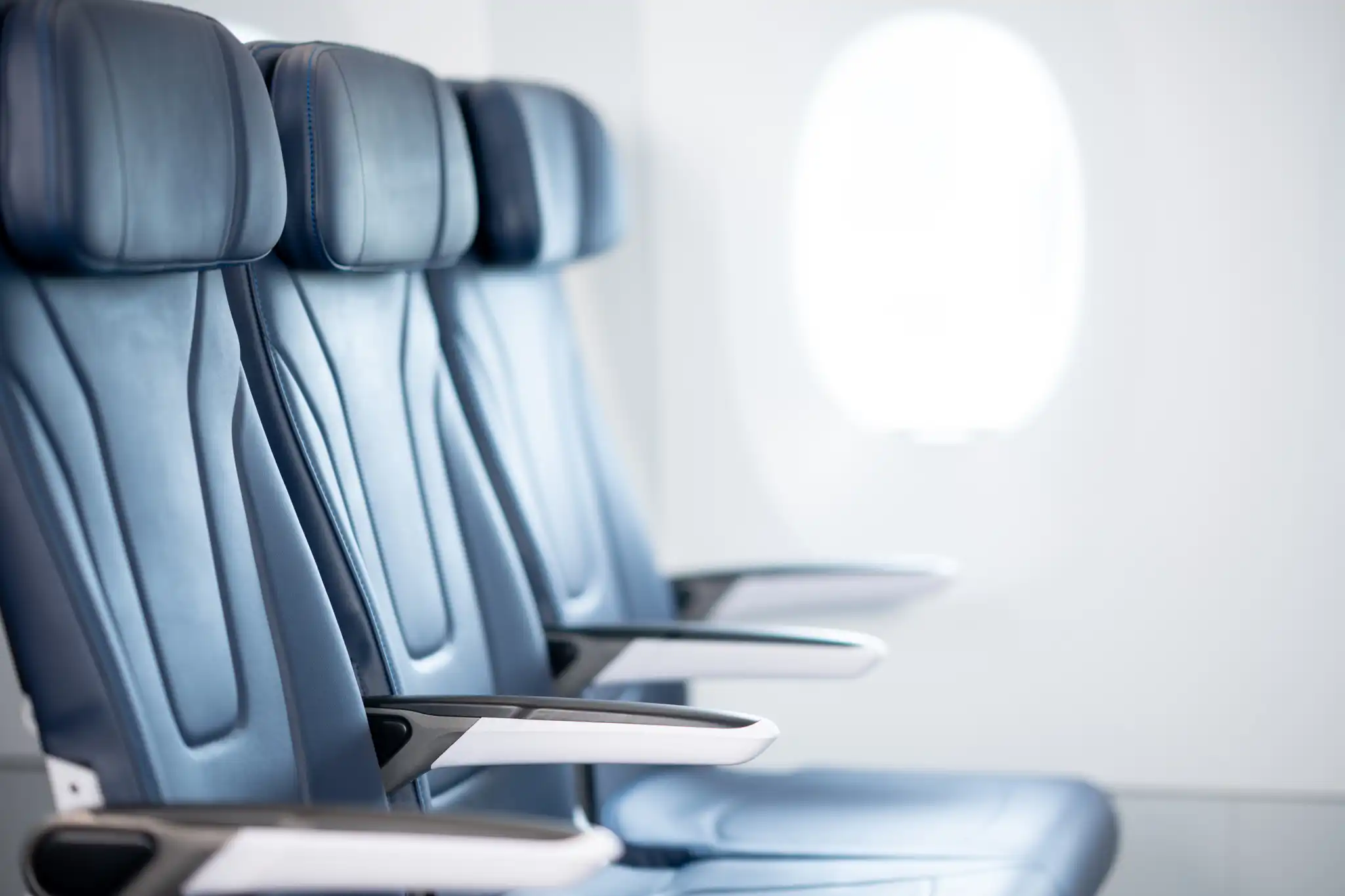 Drei blaue Ledersitze in einem Flugzeug mit einem Fenster im Hintergrund.